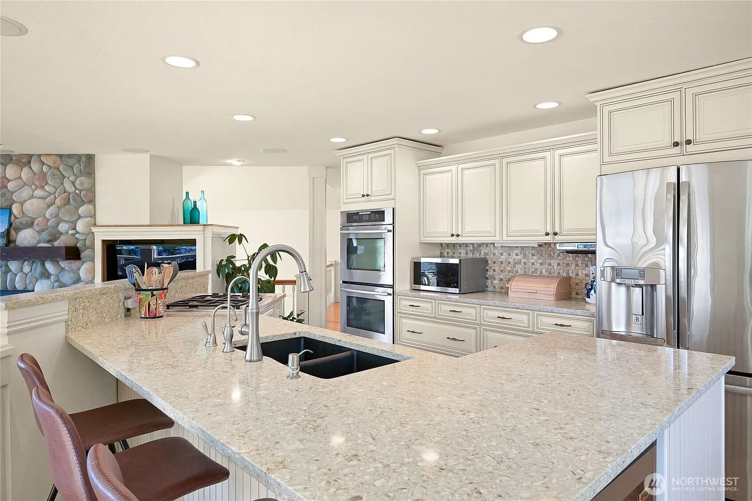 Modern kitchen with white cabinets, stainless steel appliances, and a large granite island with barstools.
