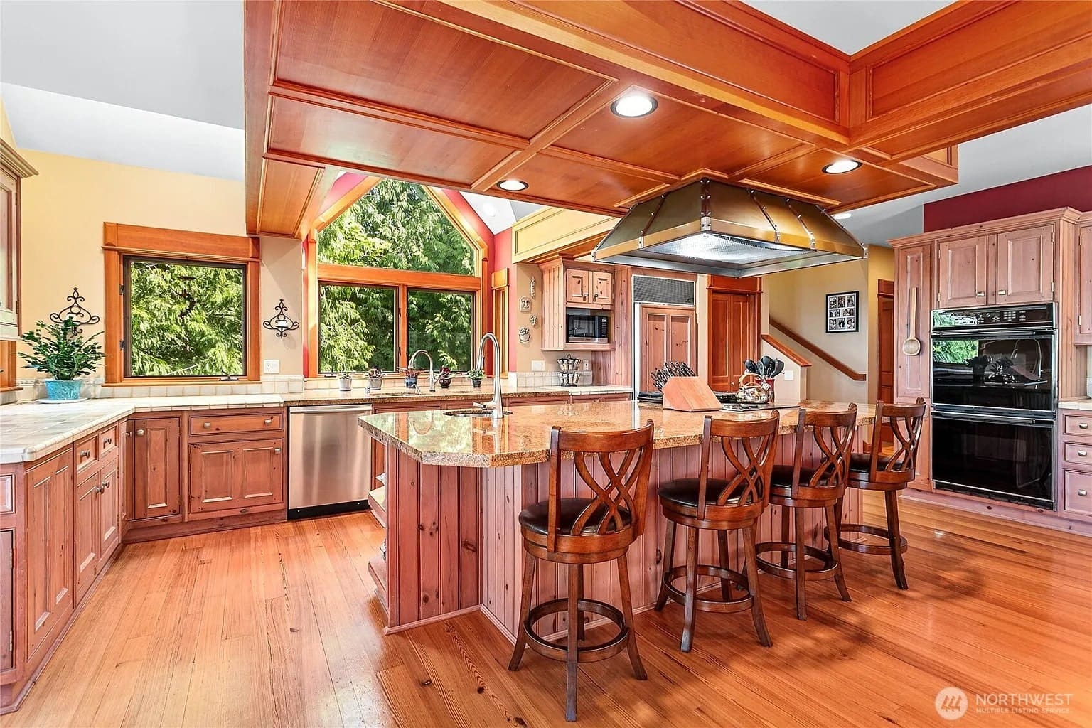 Spacious kitchen with wooden cabinets, large island, barstools, and stainless steel appliances. Bright natural light.