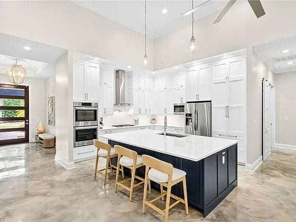 Modern kitchen with white cabinets, stainless steel appliances, large island, and three wooden bar stools.