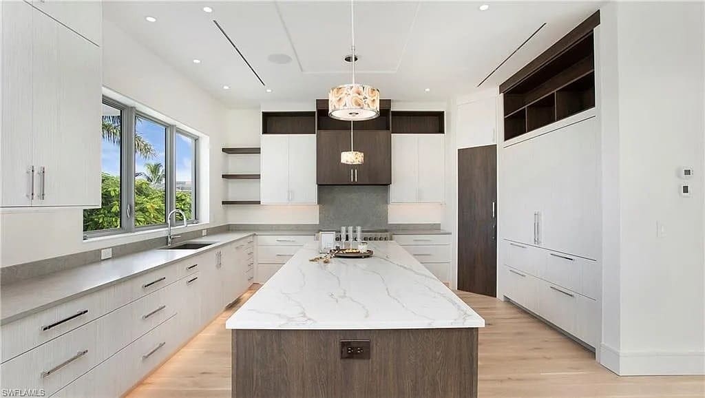 Modern kitchen with a large marble island, white cabinets, and pendant lighting.