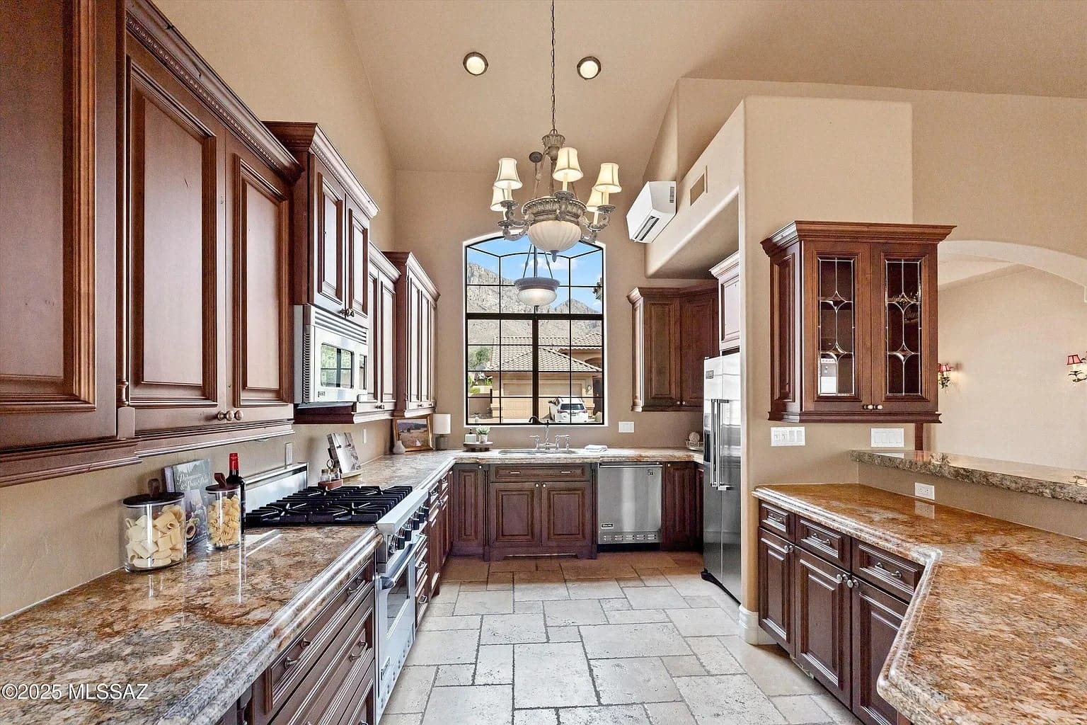 Spacious kitchen with wooden cabinets, granite countertops, chandelier, and large window providing natural light.