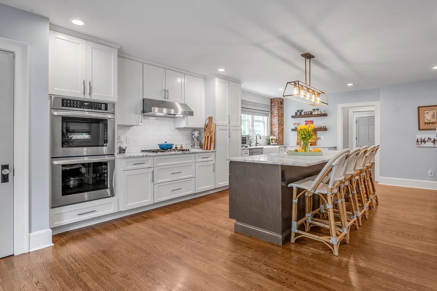 Modern kitchen with white cabinets, stainless steel appliances, island with bar stools, and wooden floor.