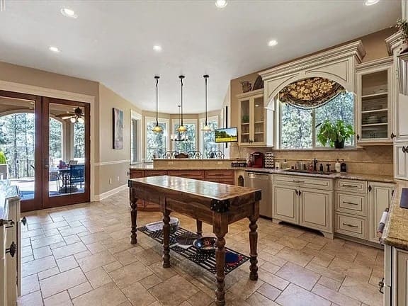 Spacious kitchen with a wooden island, white cabinets, and large windows overlooking a patio.