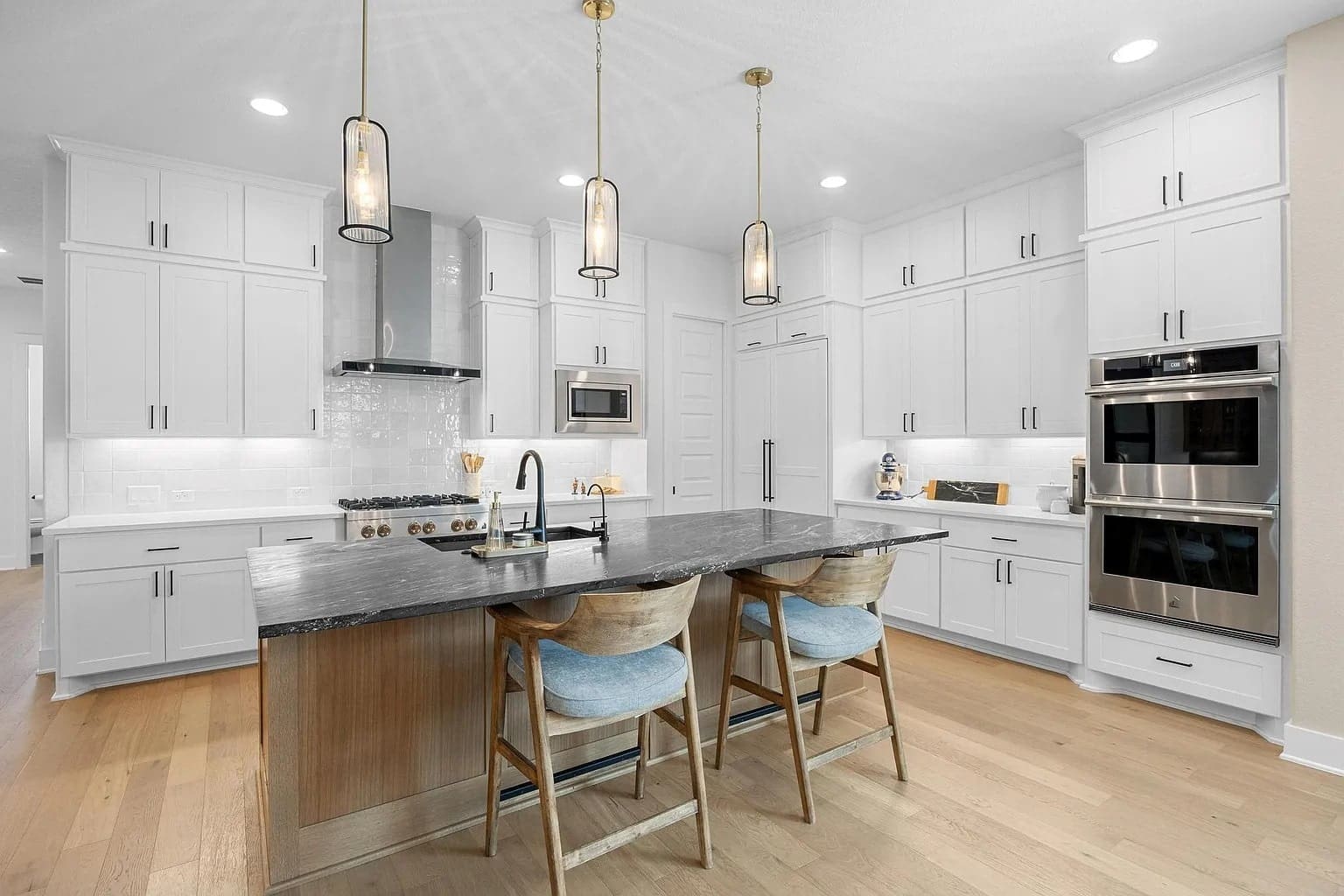 Modern kitchen with white cabinets, black island countertop, pendant lights, and stainless steel appliances.