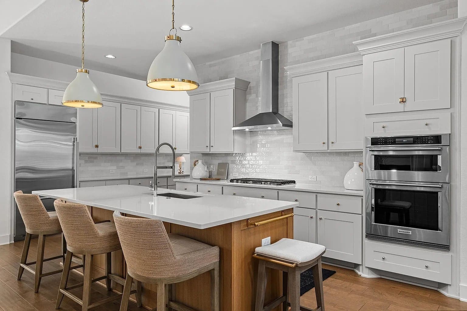Modern kitchen with white cabinets, stainless steel appliances, island with sink, and pendant lights.