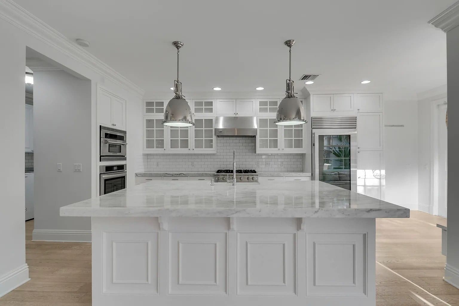 Modern kitchen with white cabinetry, marble island, stainless steel appliances, and pendant lighting.