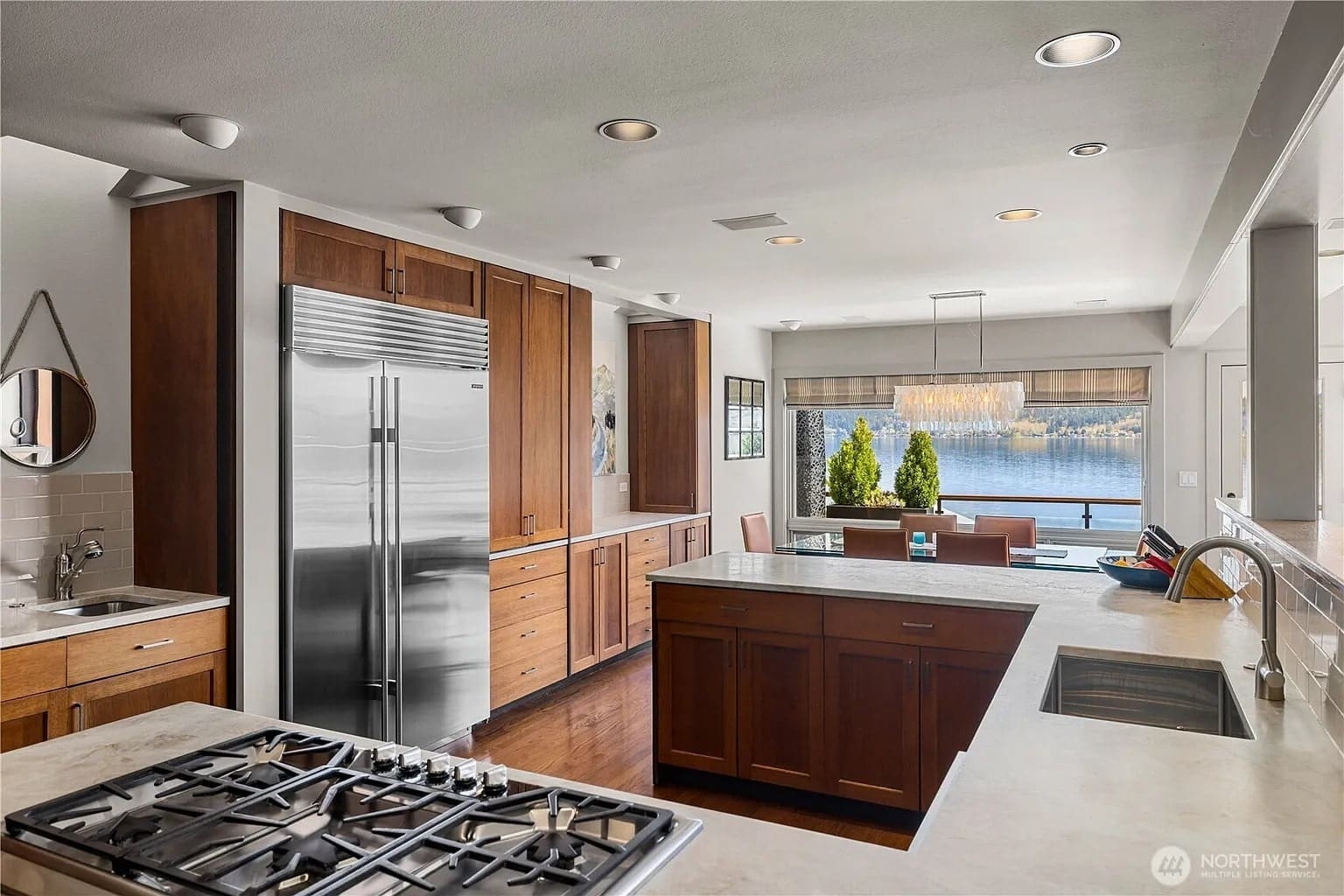 Modern kitchen with stainless steel appliances, wooden cabinets, and a view of a lake through large windows.