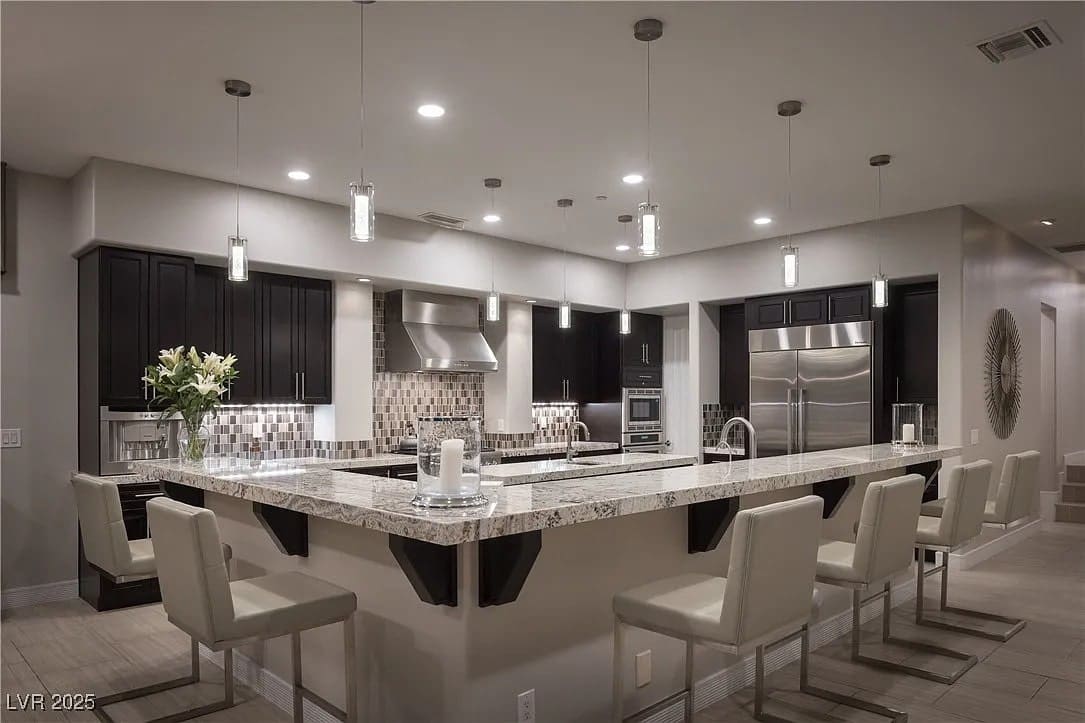 Modern kitchen with marble island, bar stools, stainless steel appliances, and pendant lighting.