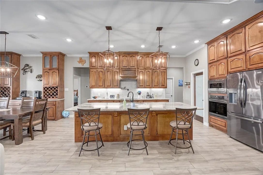 Spacious kitchen with wooden cabinets, island with barstools, stainless steel appliances, and pendant lighting.