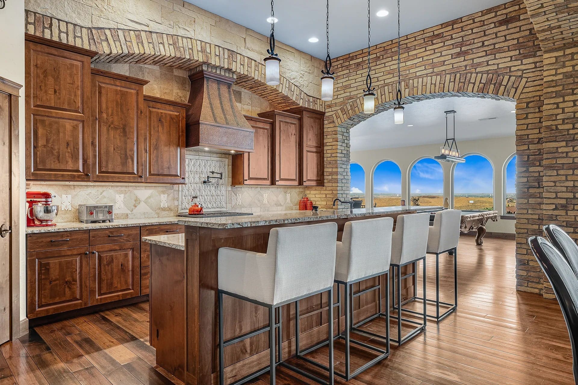 Spacious kitchen with wooden cabinets, island seating, brick arches, and large windows with scenic views.