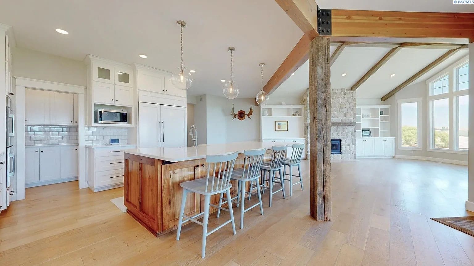 Spacious kitchen and living area with wooden beams, island, and large windows.