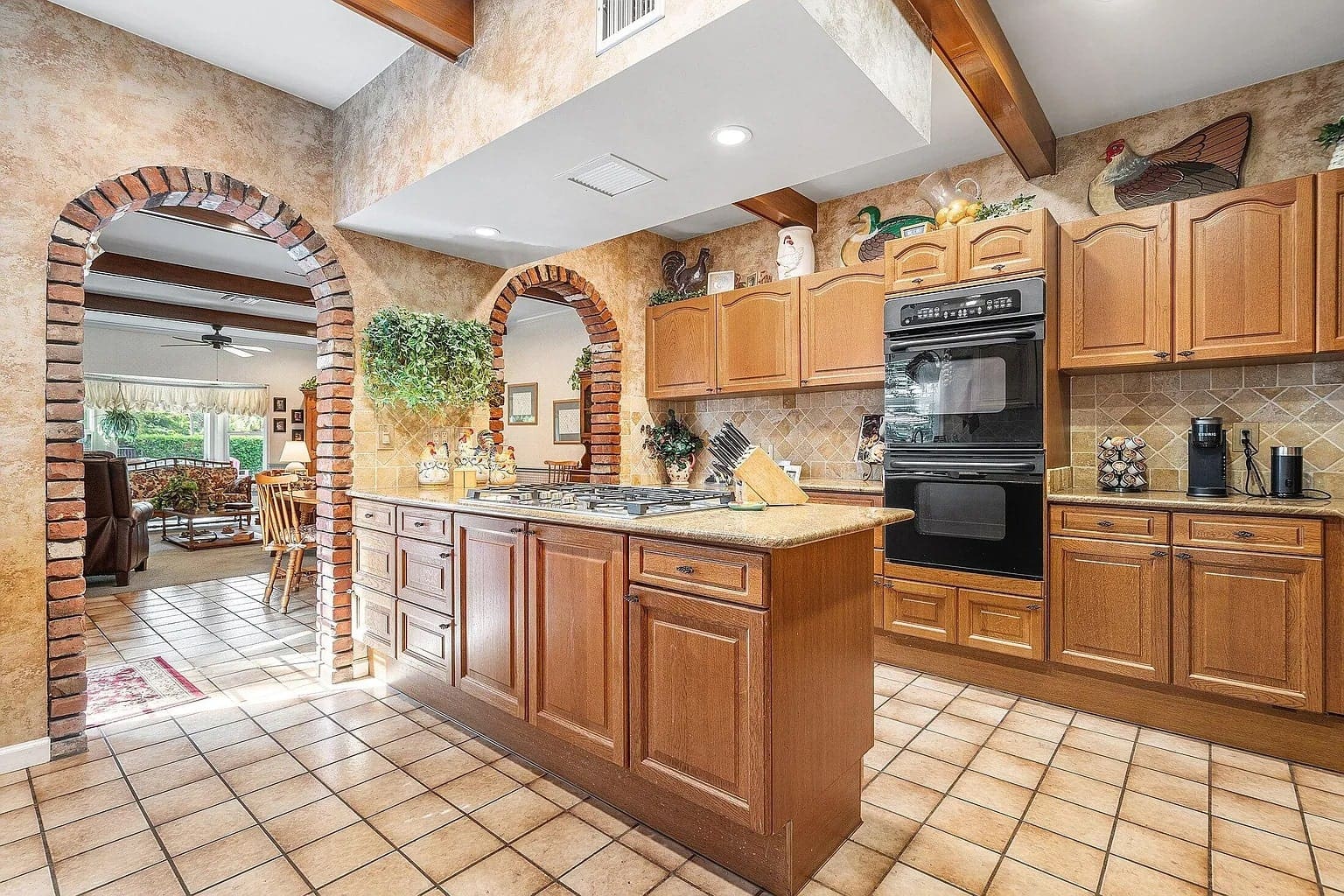 Spacious kitchen with wooden cabinets, double oven, and arched brick doorways leading to dining area.