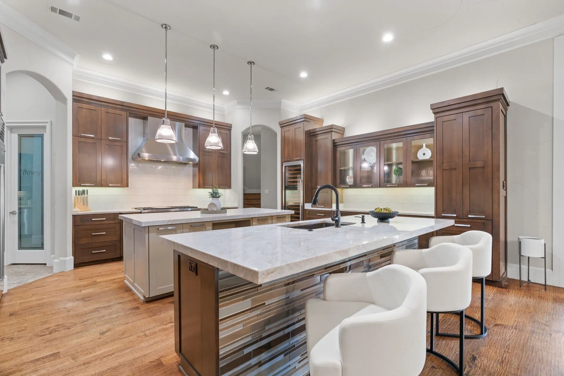 Modern kitchen with wooden cabinets, marble countertops, island with bar stools, and pendant lighting.
