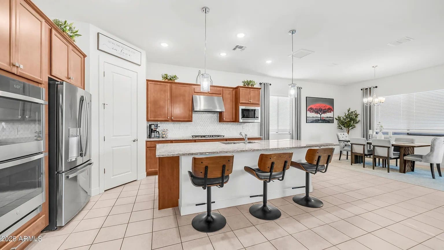 Modern kitchen with wooden cabinets, island with three stools, and adjacent dining area.