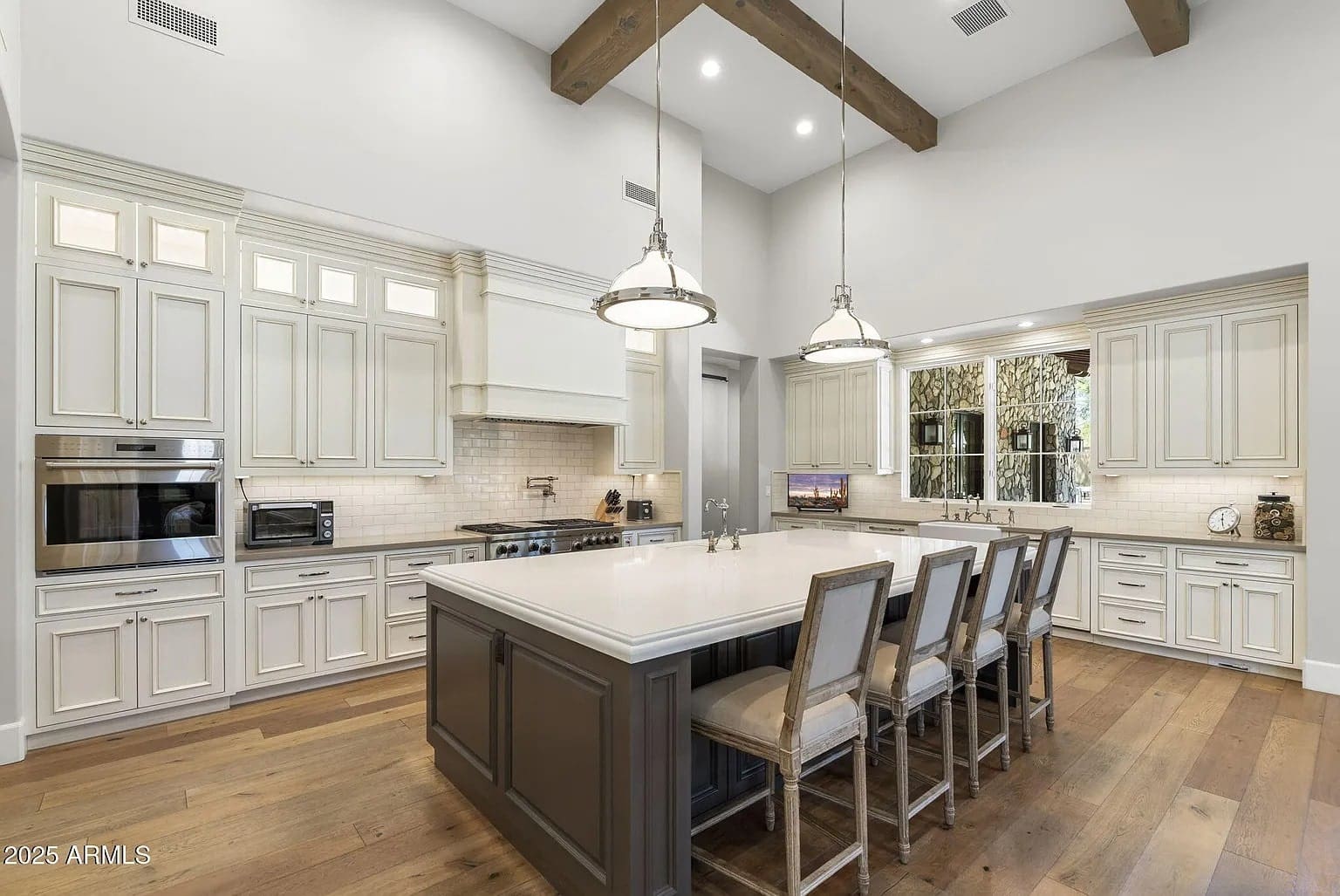 Spacious kitchen with large island, wooden beams, pendant lights, and white cabinetry.