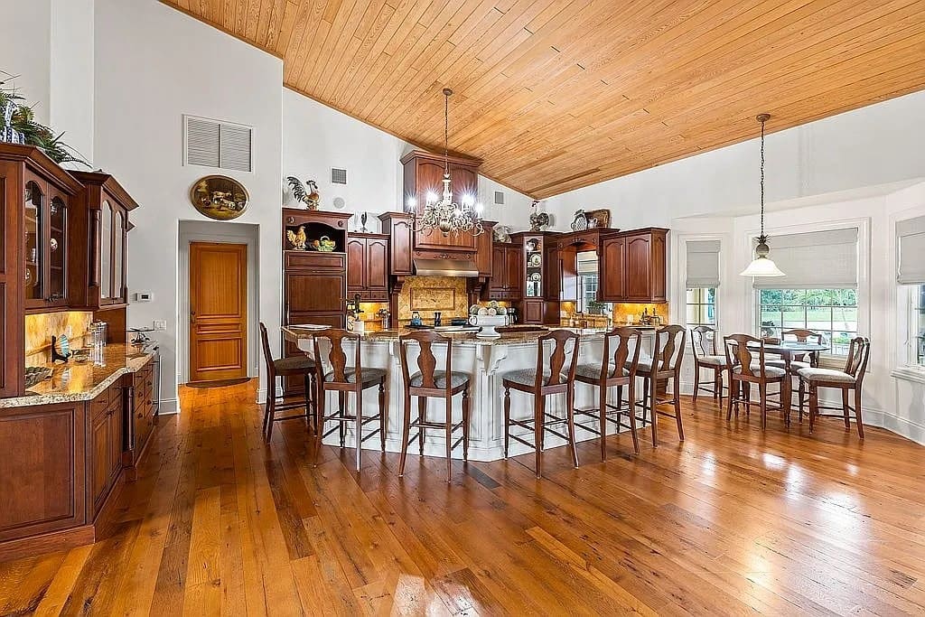 Spacious kitchen with wooden floors, large island, bar stools, and elegant chandelier.