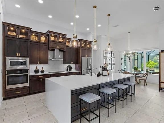 Modern kitchen with dark wood cabinets, large white island, pendant lights, and bar stools.