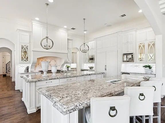 Spacious modern kitchen with white cabinets, granite countertops, and pendant lighting over an island.