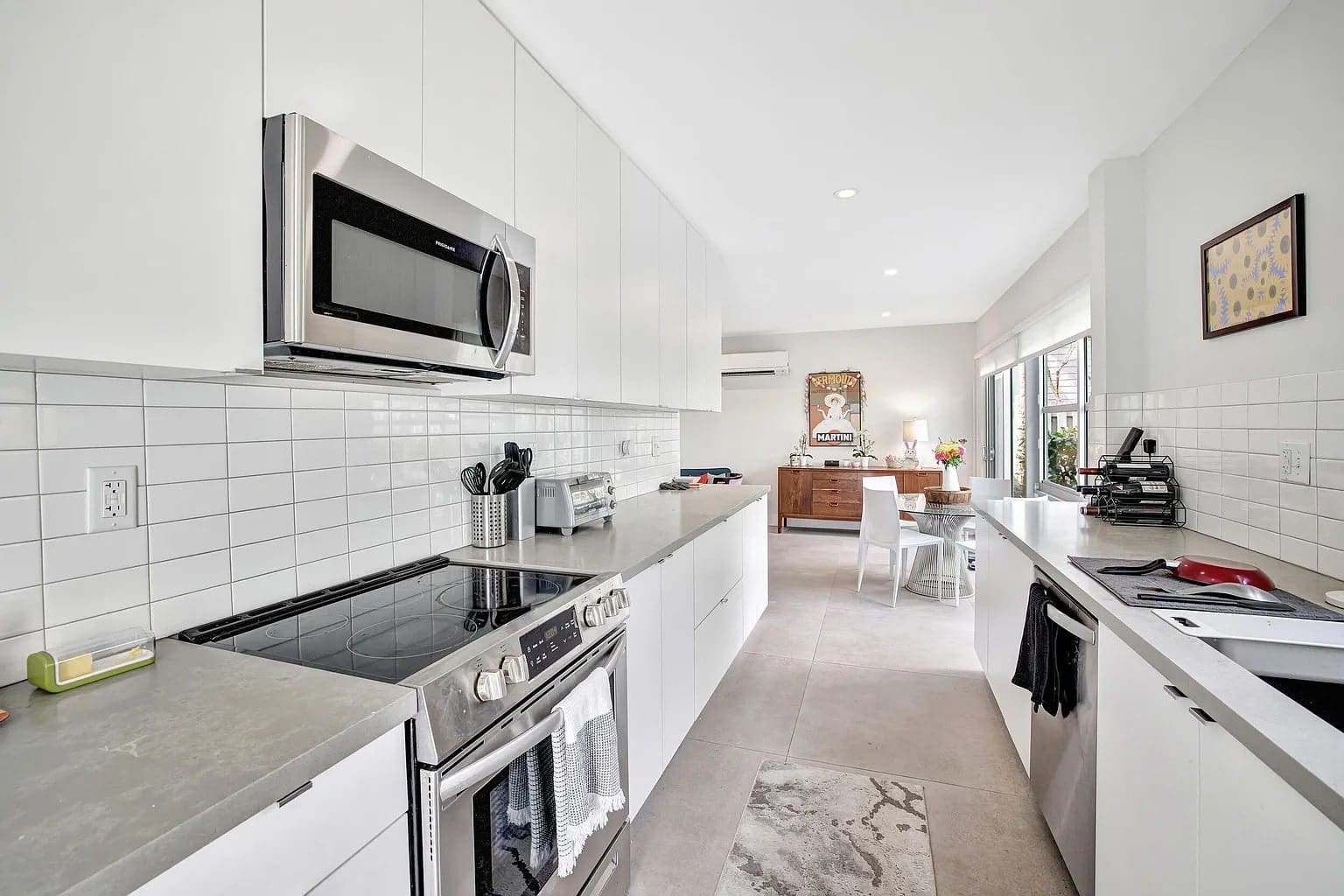 Modern kitchen with white cabinets, stainless steel appliances, and a dining area in the background.