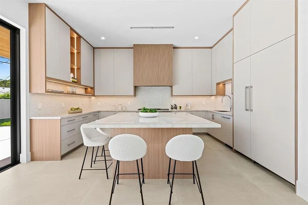 Modern kitchen with white cabinets, wooden accents, island with stools, and large windows.