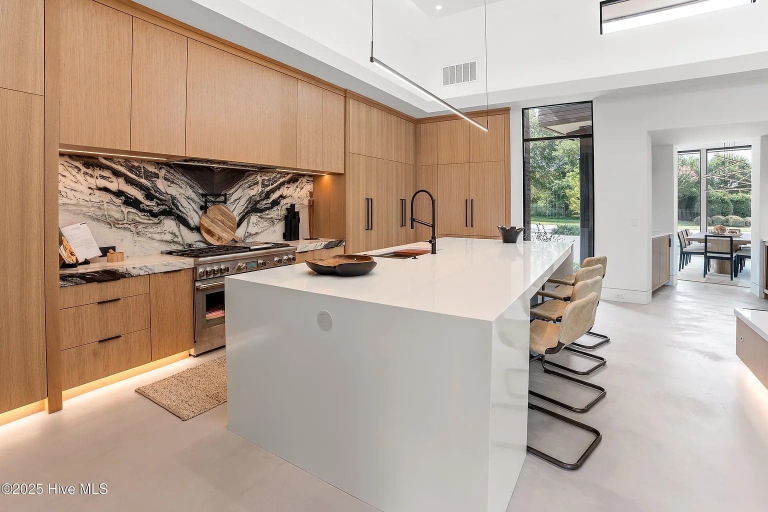 Modern kitchen with wood cabinetry, large white island, marble backsplash, and seating for four.
