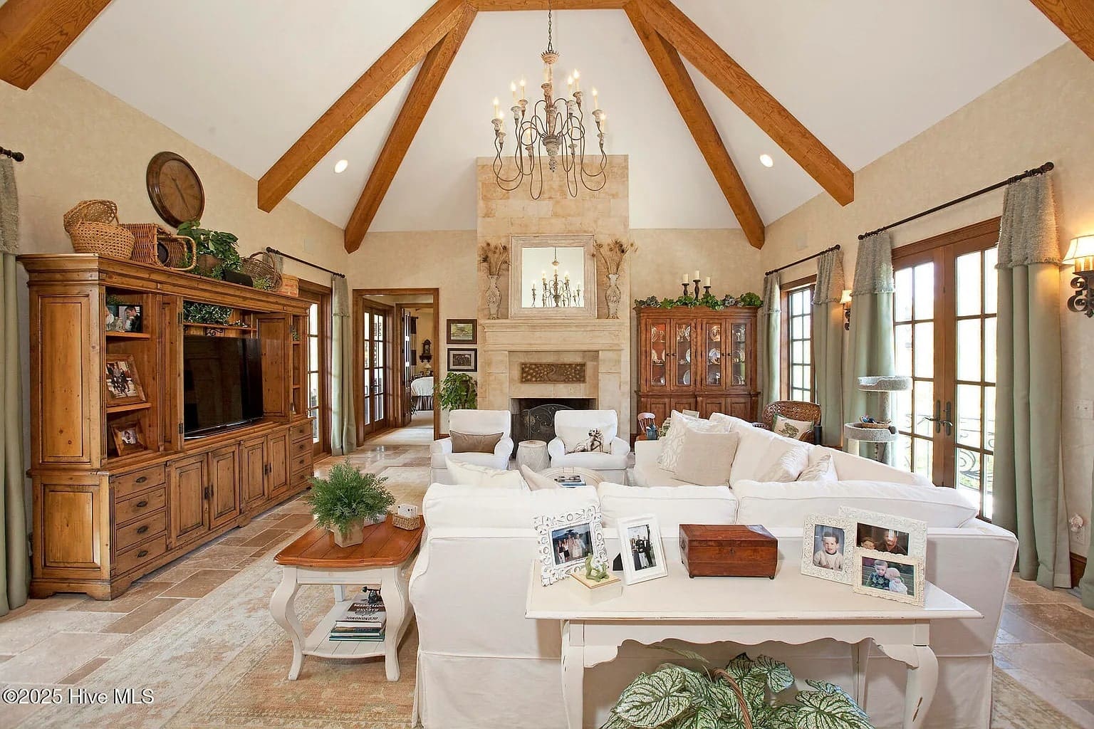 Spacious living room with vaulted ceiling, chandelier, white sofas, fireplace, and wooden furniture.