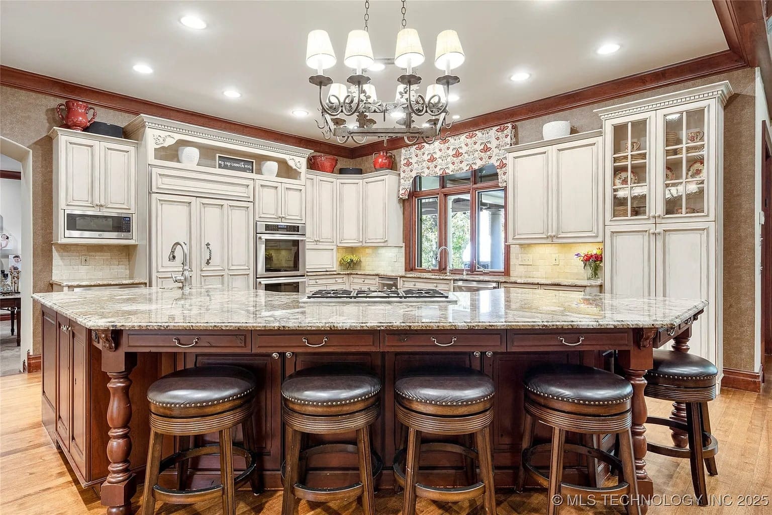 Spacious kitchen with a large island, chandelier, white cabinets, and bar stools.