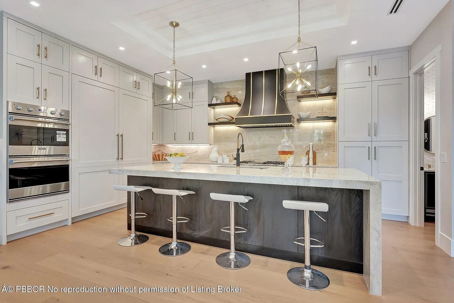 Modern kitchen with marble island, four stools, pendant lights, and stainless steel appliances.