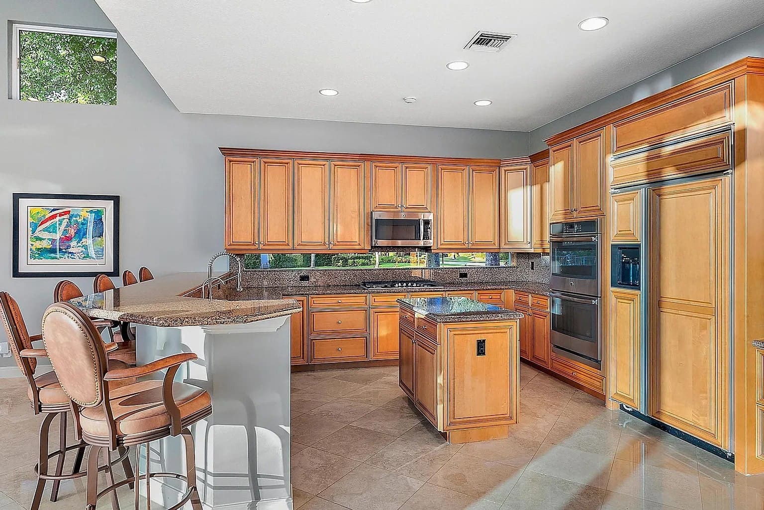 Spacious kitchen with wooden cabinets, island, bar seating, and modern appliances under recessed lighting.