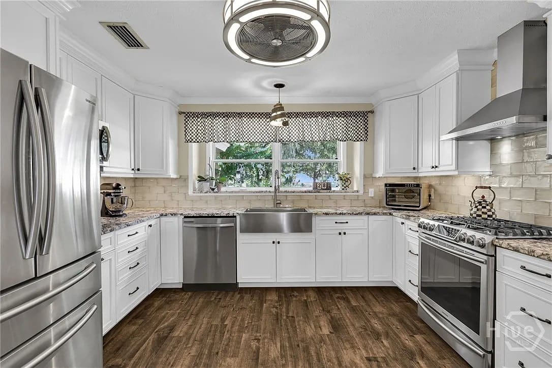 Modern kitchen with white cabinets, stainless steel appliances, farmhouse sink, and wooden floor.
