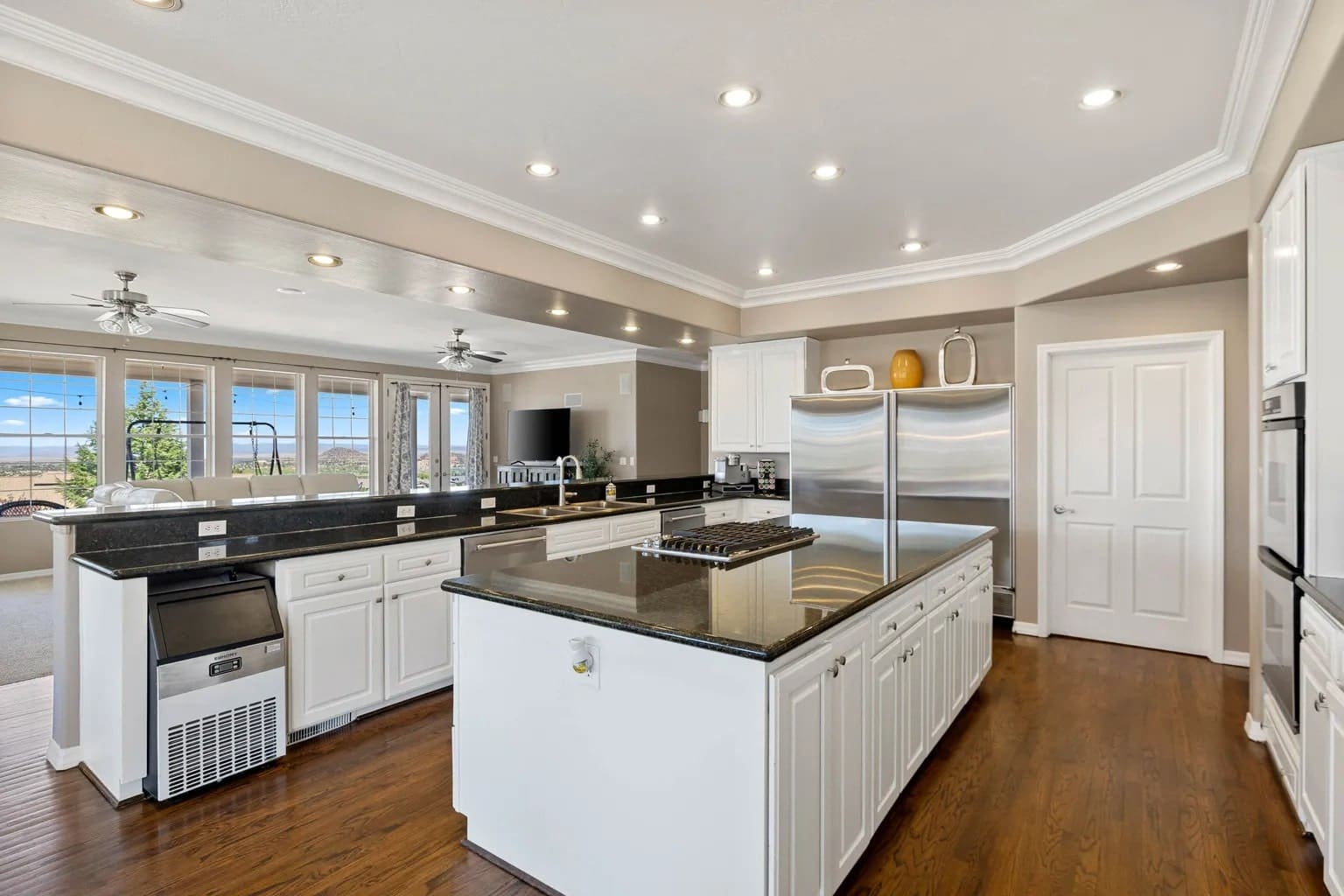 Spacious modern kitchen with white cabinets, black countertops, stainless steel appliances, and hardwood floors.
