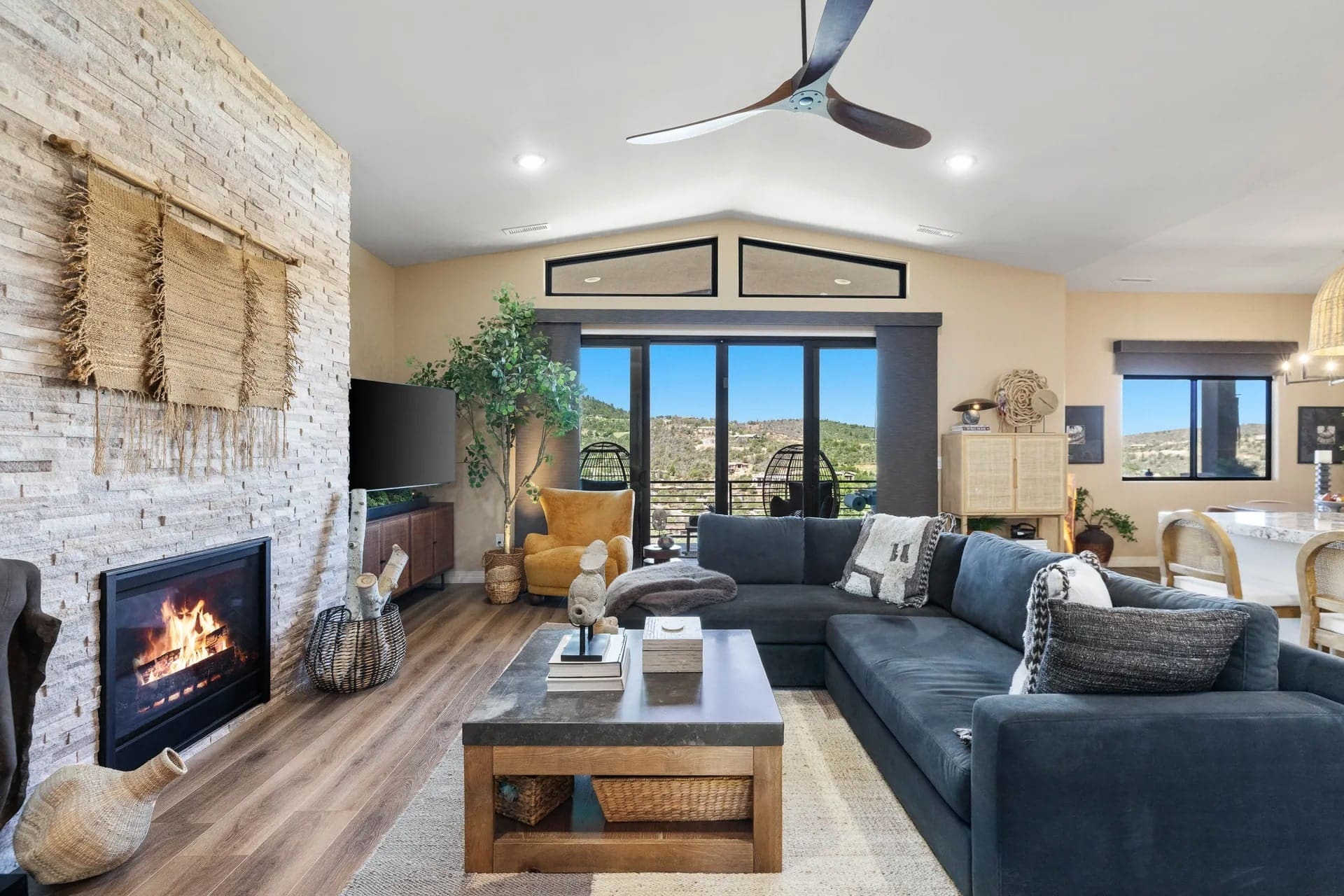 Modern living room with a fireplace, large sectional sofa, and a view of mountains through windows.