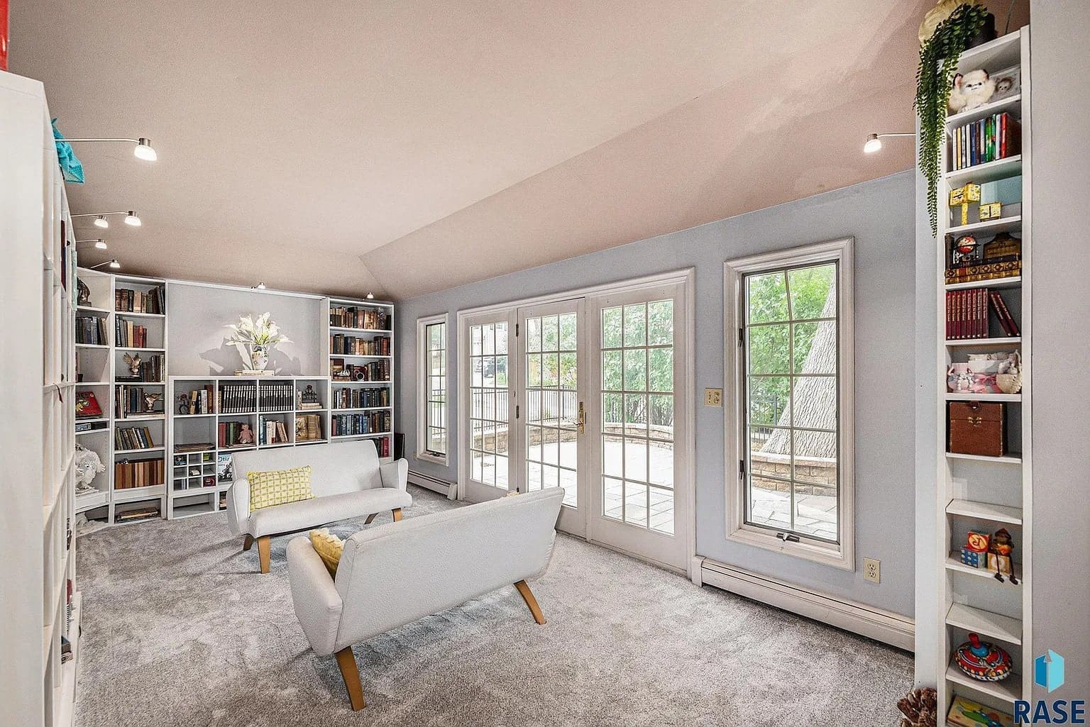 Bright room with bookshelves, two white chairs, and large windows overlooking a patio.