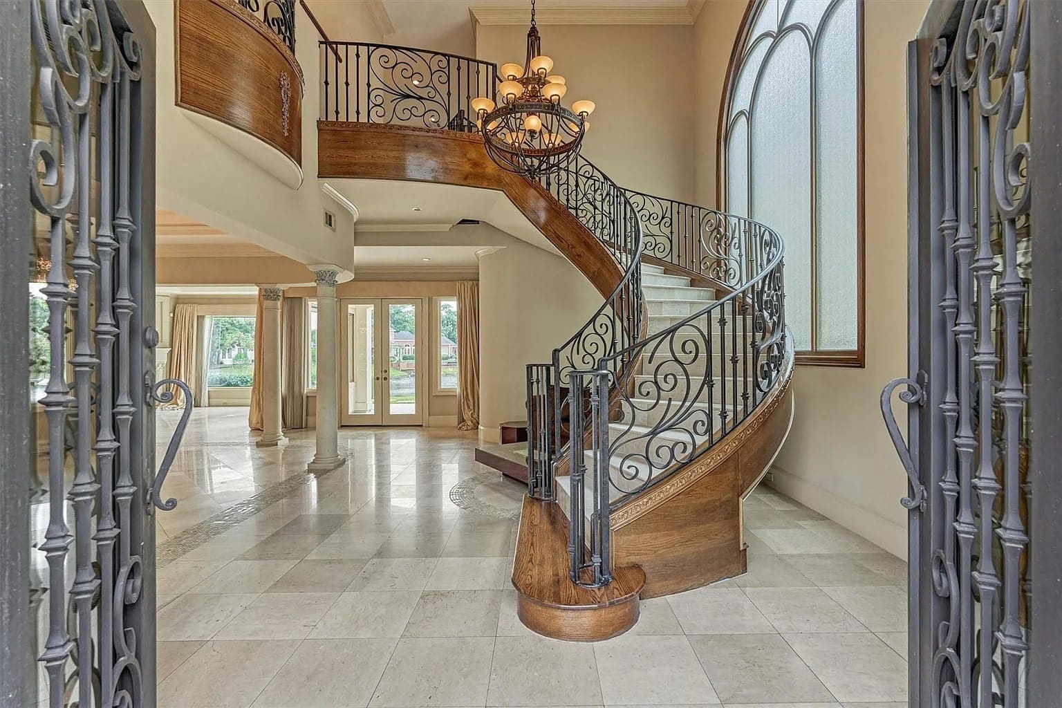 Elegant foyer with a grand, curved wooden staircase and ornate iron railings.
