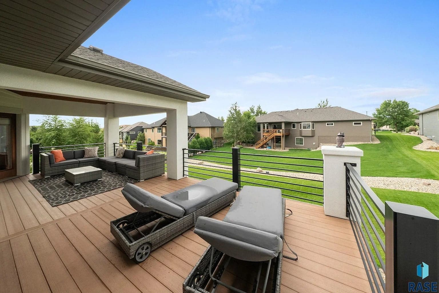 Spacious backyard deck with lounge chairs, outdoor seating, and view of neighboring houses and green lawn.
