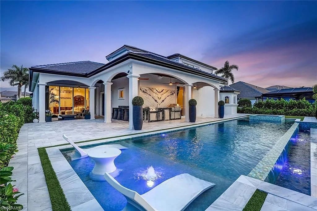 Luxury modern house with a pool, outdoor kitchen, and evening lighting.