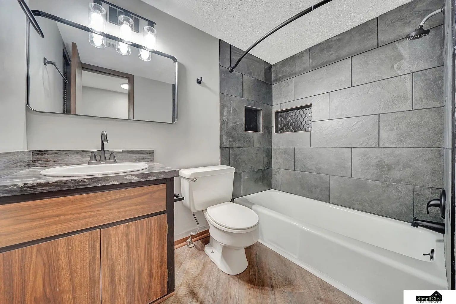 Modern bathroom with dark tiled shower, white bathtub, toilet, and wooden vanity with a mirror.
