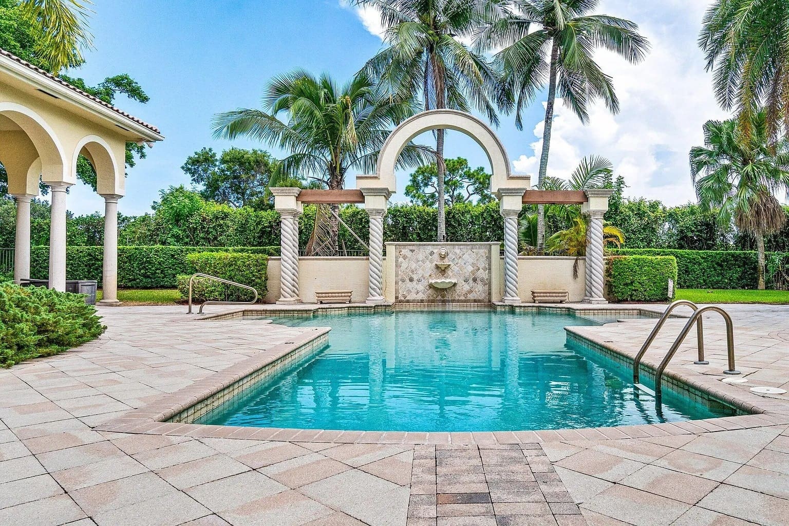Luxurious outdoor pool with decorative arches and palm trees, surrounded by a tiled patio.
