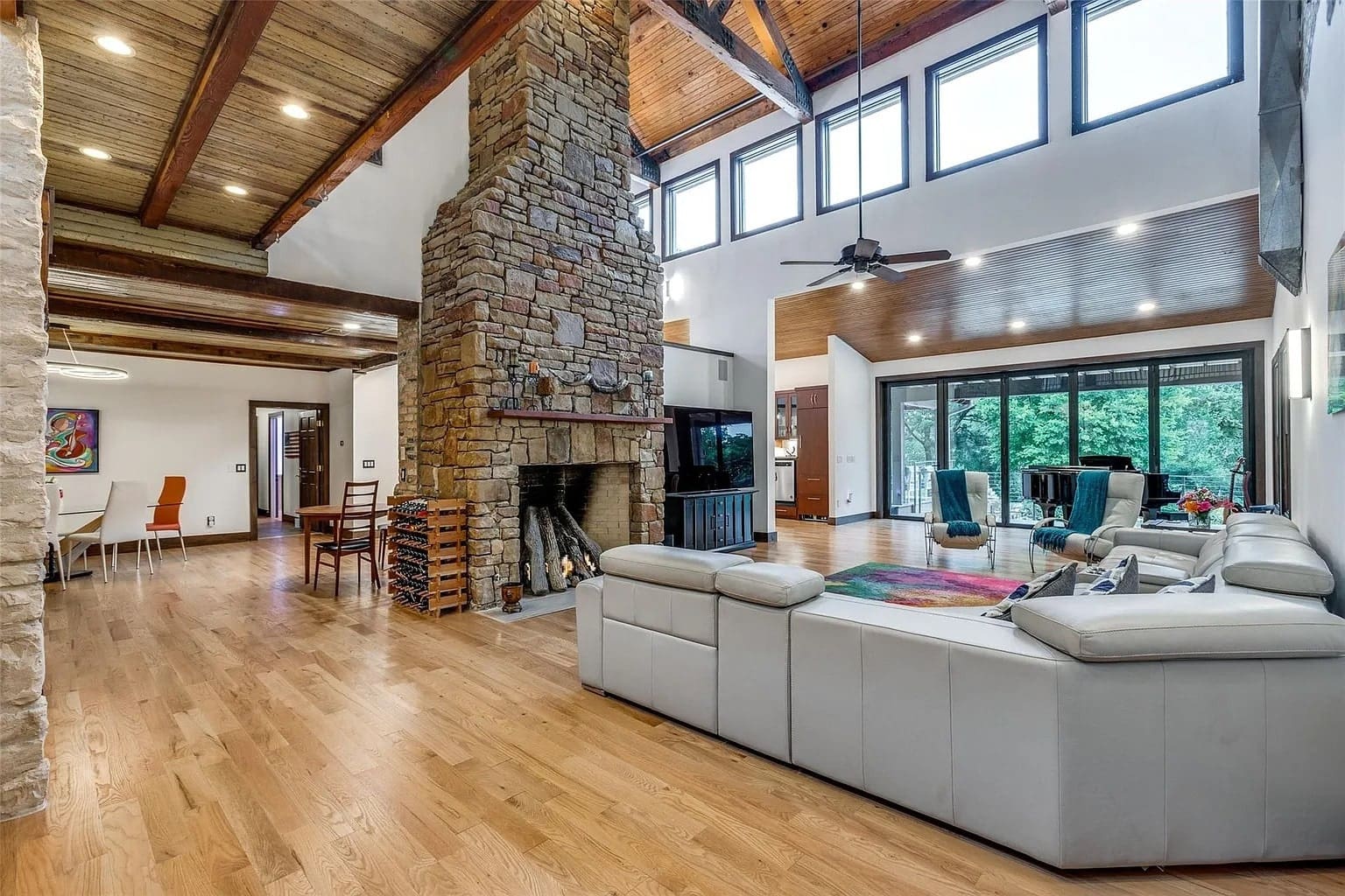 Spacious living room with high ceilings, stone fireplace, and large windows overlooking greenery.
