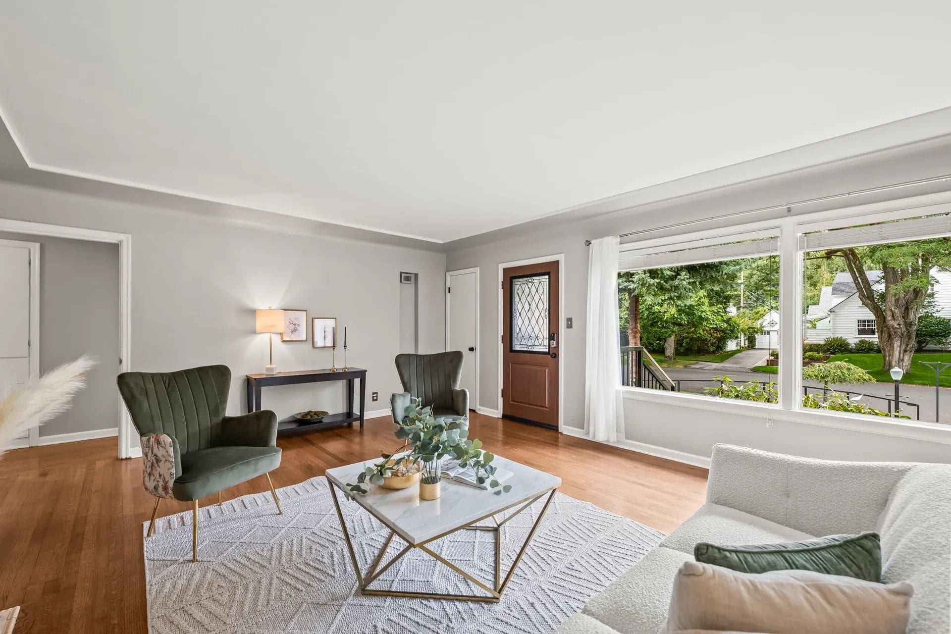 Spacious living room with modern furniture, large window, and wooden floor, overlooking a garden.
