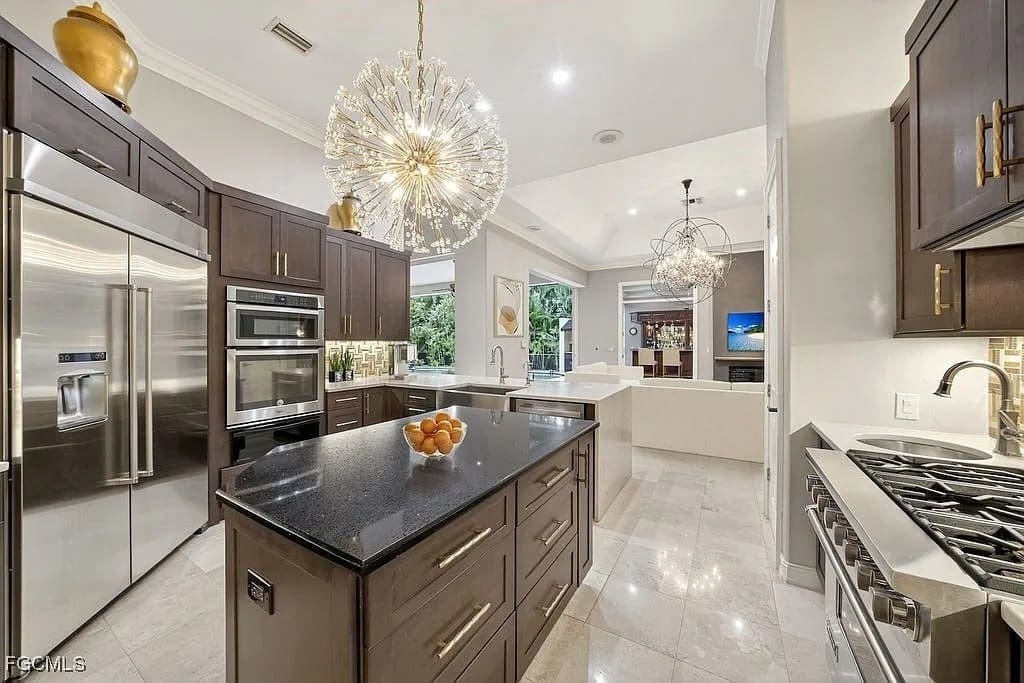 Modern kitchen with dark wood cabinets, stainless steel appliances, and a central island with fruit bowl.
