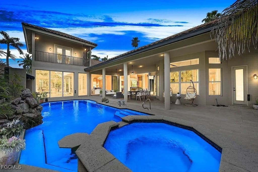 Modern house with large windows, outdoor patio, and illuminated pool at twilight.
