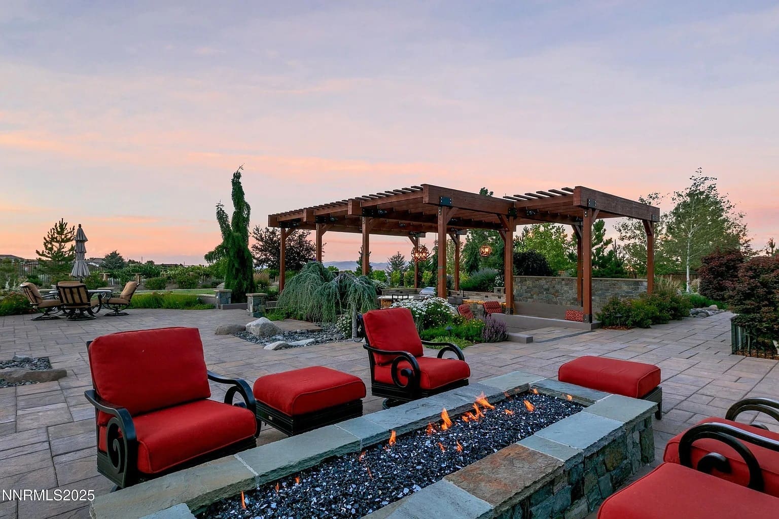 Patio with red cushioned chairs, fire pit, and wooden pergola at sunset.