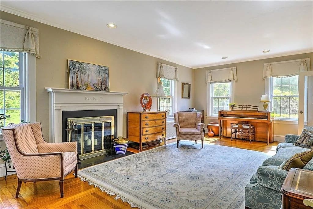 Elegant living room with fireplace, piano, armchairs, and large rug on wooden floor.

