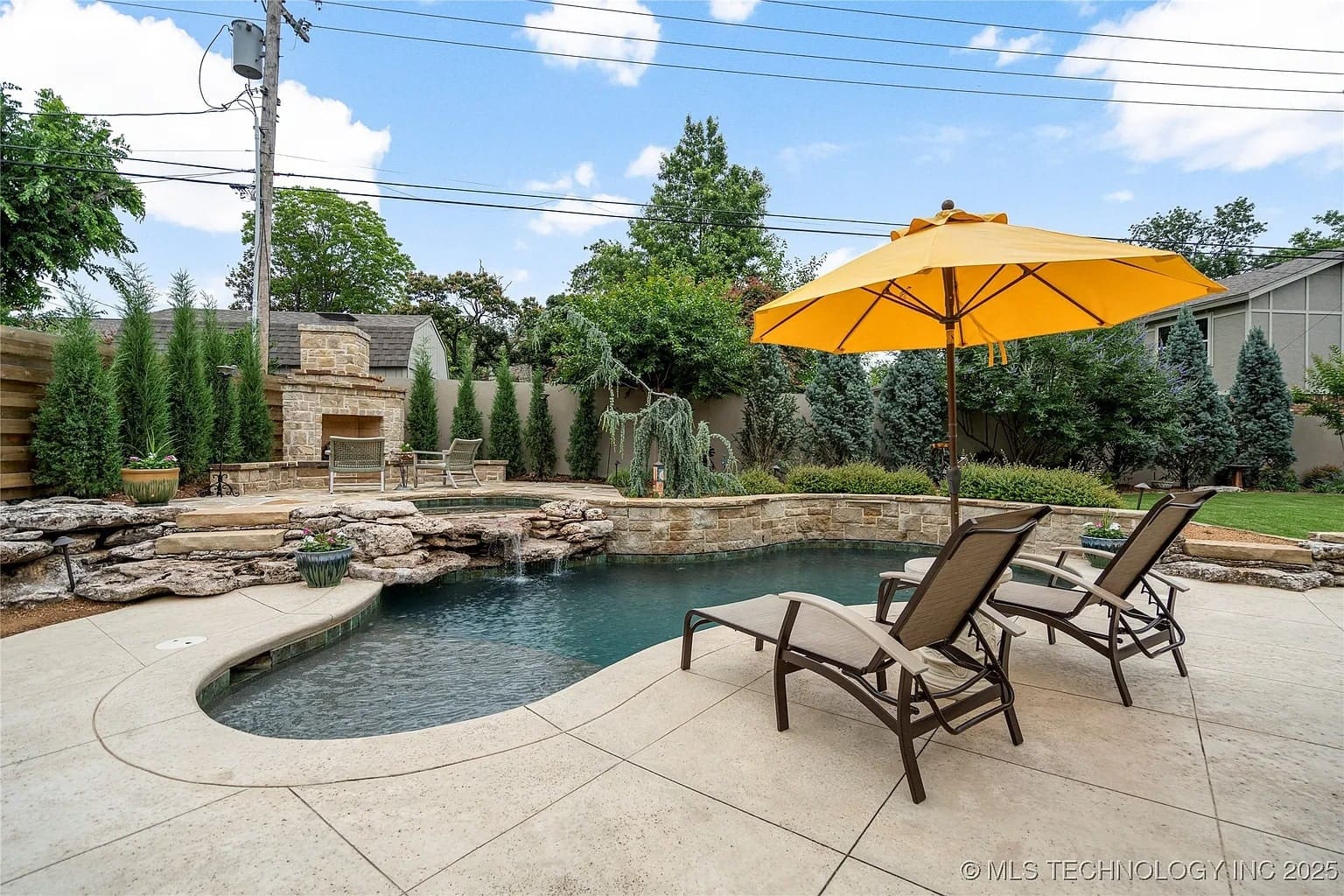 Backyard with a pool, stone fireplace, lounge chairs, and a yellow umbrella.

