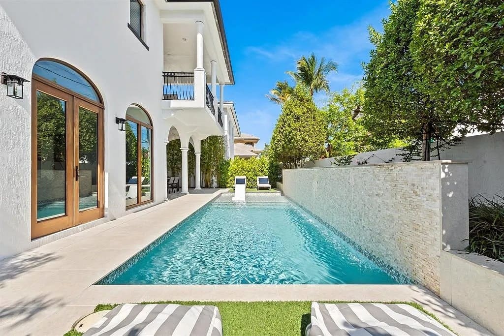 Modern house with a pool, surrounded by greenery and lounge chairs on the patio.
