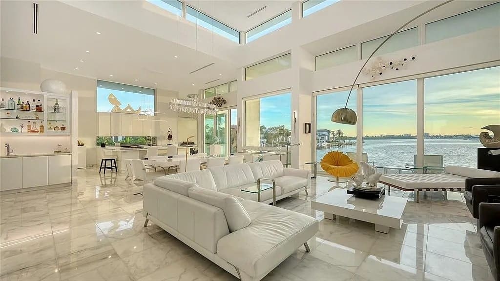 Spacious modern living room with white furniture, large windows, and a view of the water.