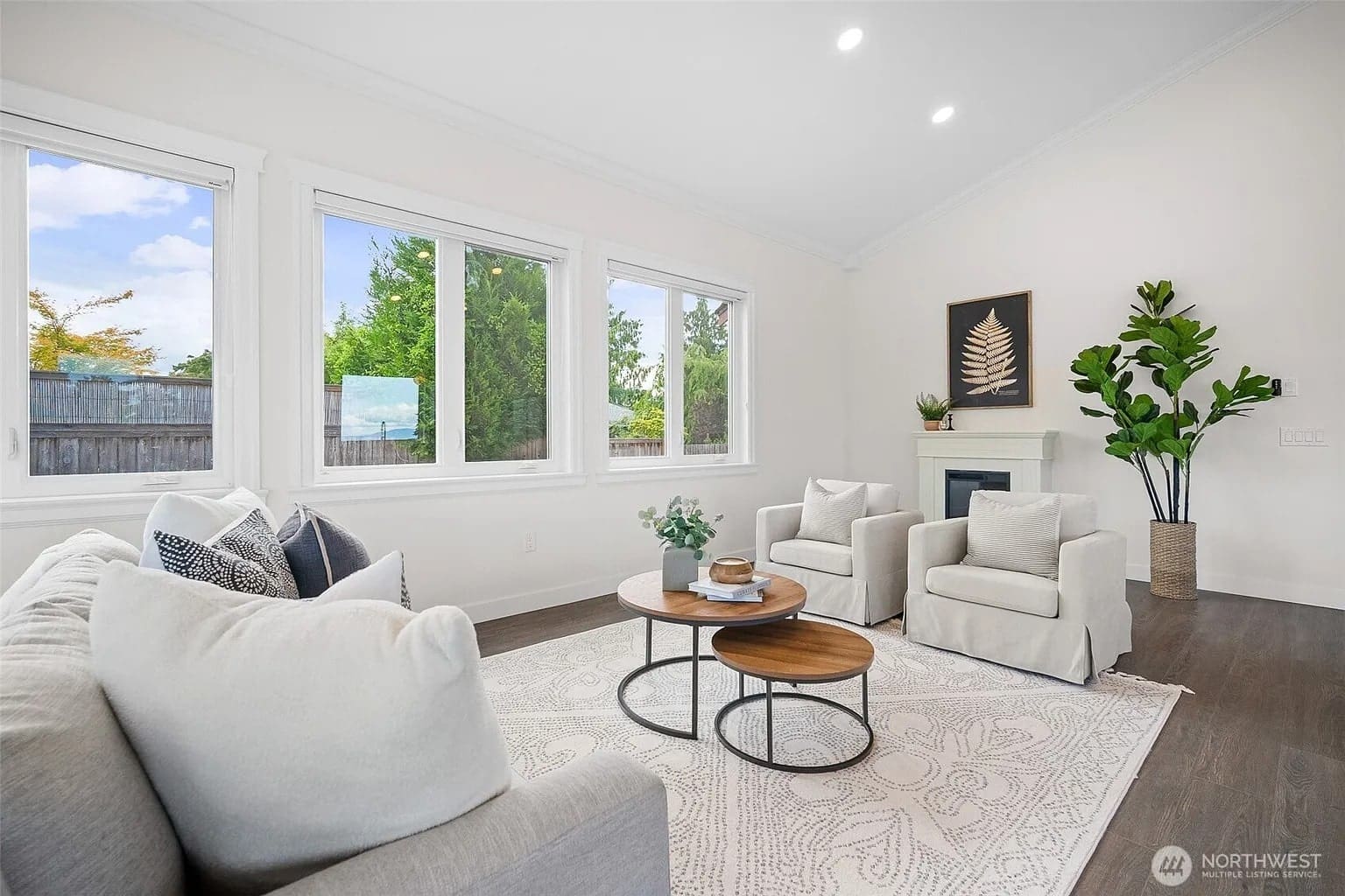 Bright living room with a white sofa, two armchairs, coffee table, and large windows.

