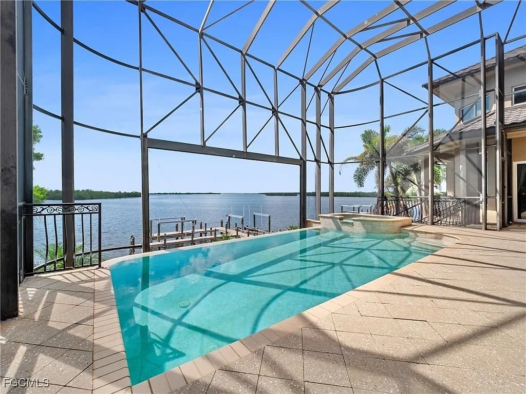 Screened-in pool area overlooking a lake with a dock and clear blue sky.
