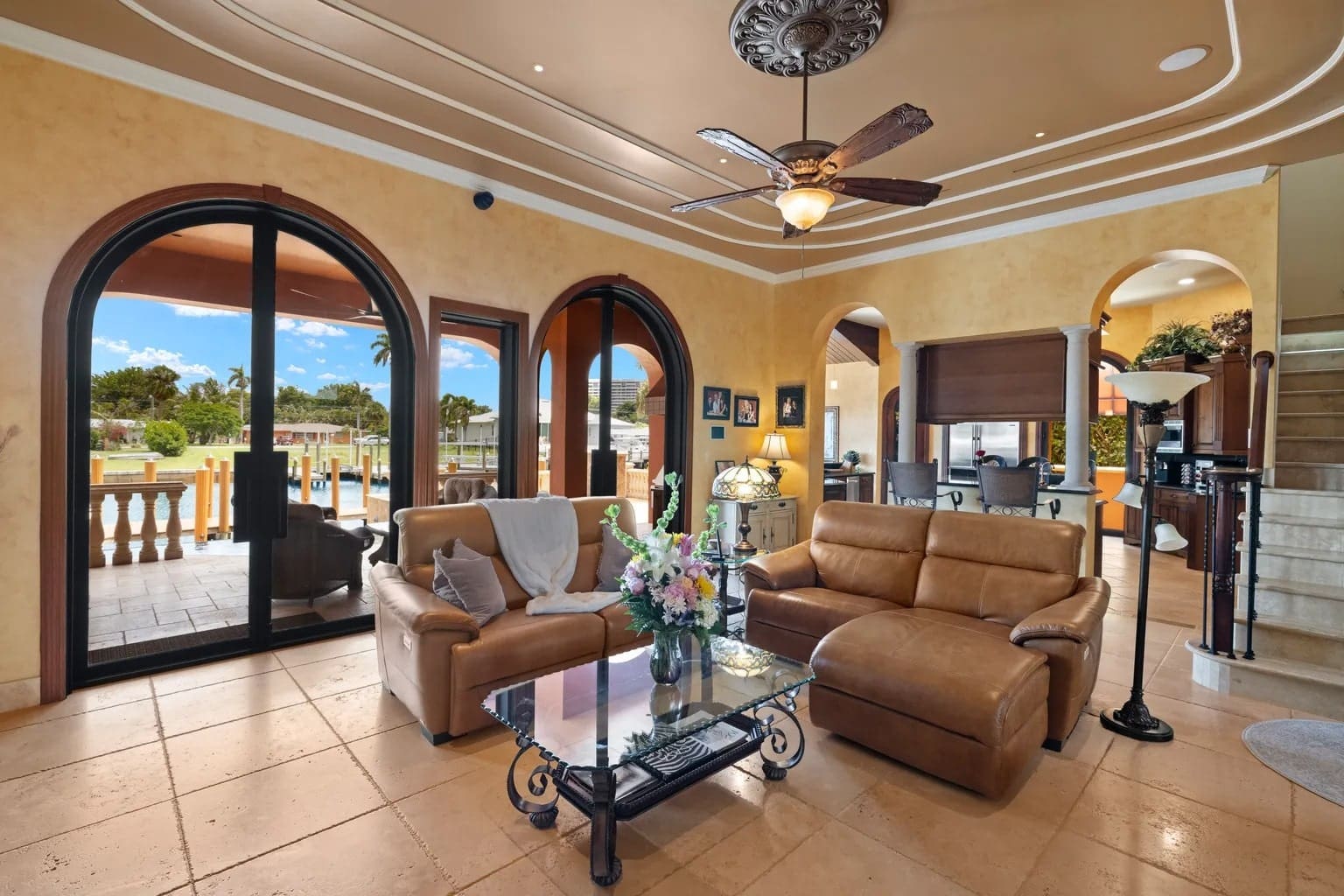 Luxurious living room with leather sofas, glass coffee table, and arched windows overlooking a pool.
